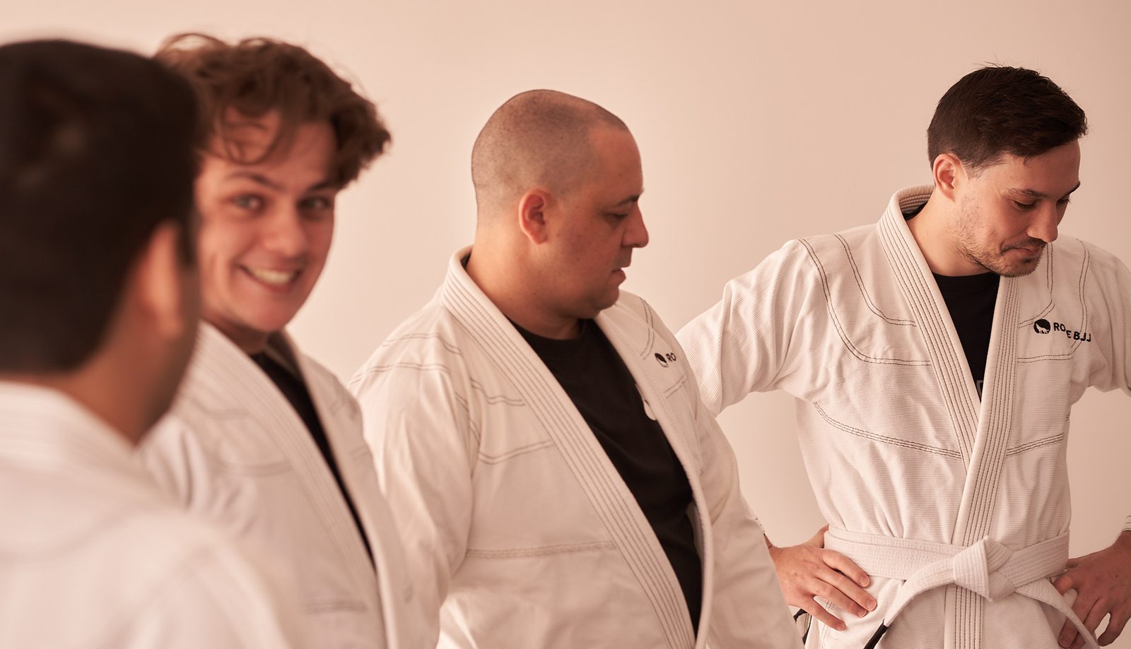 Four students stand together before class, one tying on his white belt.