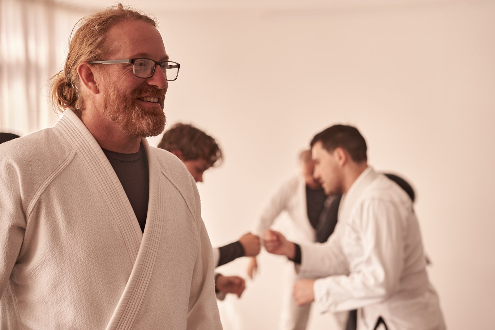 Mike Armstrong smiling on the mats, with two students bumping fists behind him before they roll.