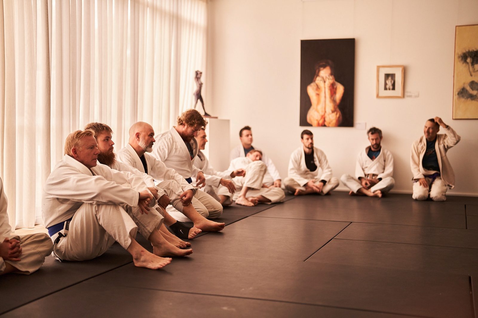 A row of students in gis sits cross-legged listening to the instructor.