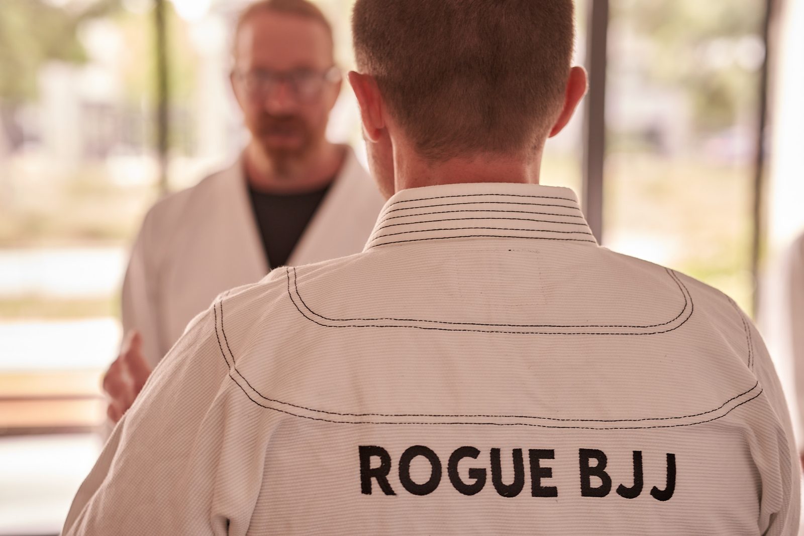 Two members talk near the studio's glass doors with greenery outside.