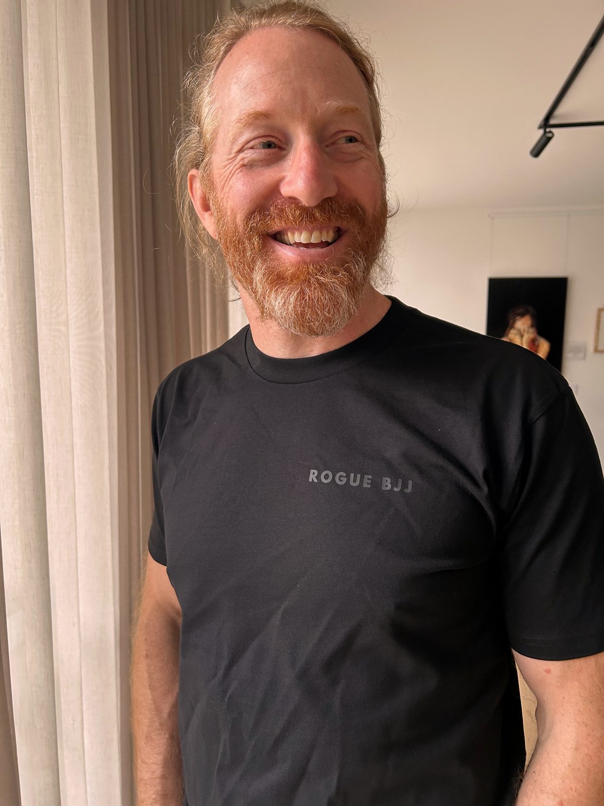 A plain black t-shirt with a small Rogue BJJ wordmark printed across the chest in grey.