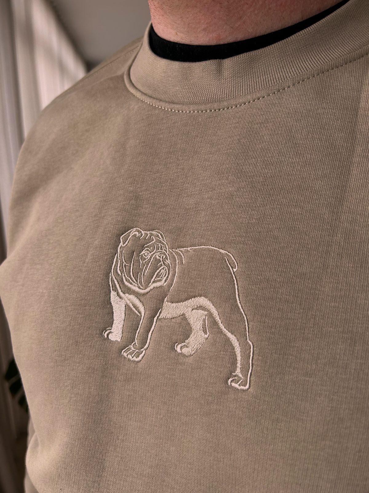 A sand-coloured crew neck jumper with a small embroidered bulldog on the chest.