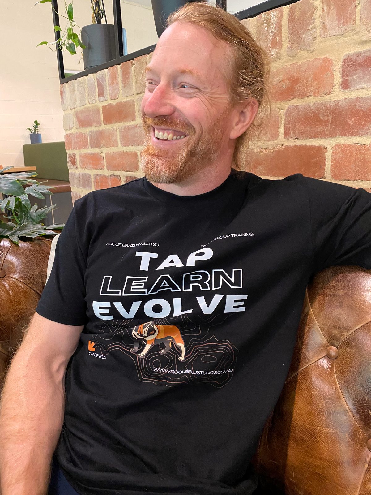 A black t-shirt with the words Tap Learn Evolve above an orange and white bulldog on a contour-line background.